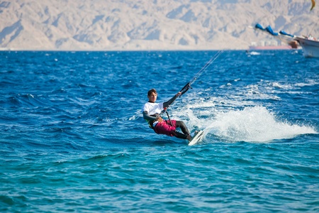 Kite surfing on the sea. The beautiful suntanned young guy goes for a drive on a board by the seaの写真素材