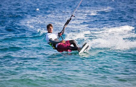 Kite surfing on the sea. The beautiful suntanned young guy goes for a drive on a board by the seaの写真素材