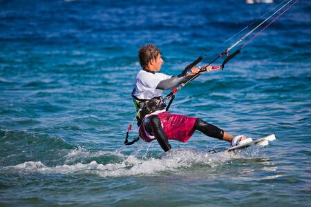 Kite surfing on the sea. The beautiful suntanned young guy goes for a drive on a board by the seaの写真素材
