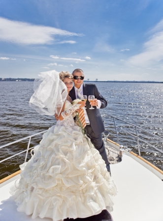 Happy groom and the bride with champagne on the yacht in solar and bright dayの写真素材