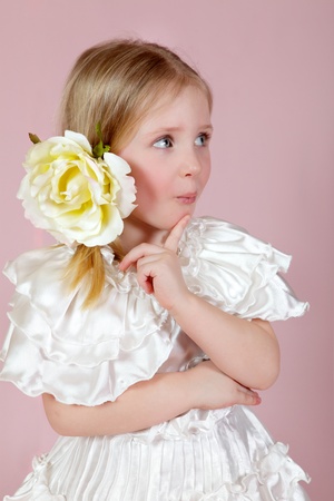 Portrait of the child in a white dress with a flower in hair on a pink background in studioの写真素材