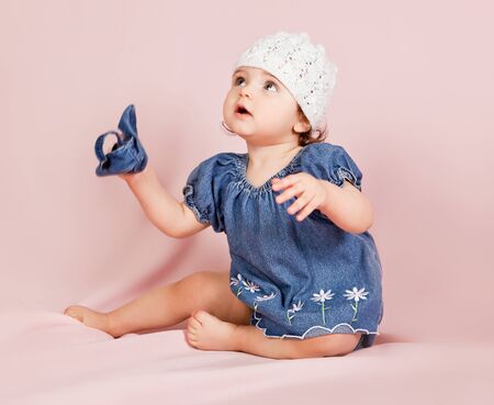 Portrait of a little girl in stylish clothing sitting on pink background and playing upの写真素材