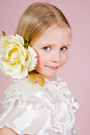 Portrait of the child in a white dress with a flower in hair on a pink background in studioの写真素材