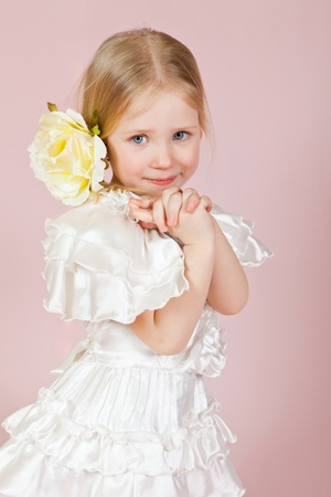 Portrait of the child in a white dress with a flower in hair on a pink background in studioの写真素材