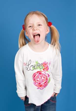 Portrait of the emotional child who is putting out the tongue in studio on a dark blue backgroundの写真素材