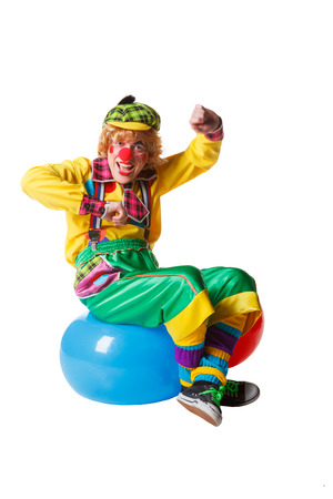 Funny clown sits on blue ball isolated on white backgroundの写真素材