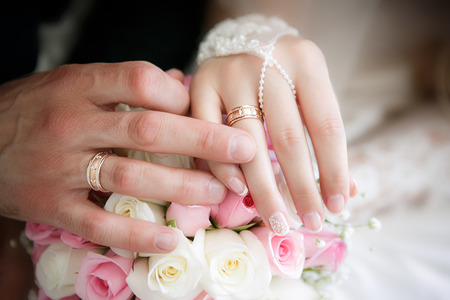 Hands of the groom and the bride with wedding rings and a wedding bouquet from rosesの写真素材