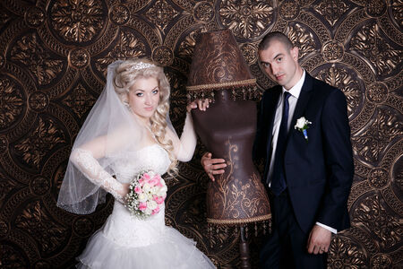 happy groom and the charming bride with a bouquet from roses in studio on a brown backgroundの写真素材