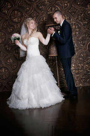 happy groom and the charming bride with a bouquet from roses in studio on a brown backgroundの写真素材