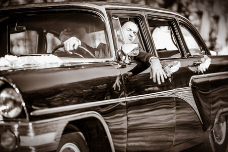 Cheerful groom at a wheel of a black old retro of the carの写真素材