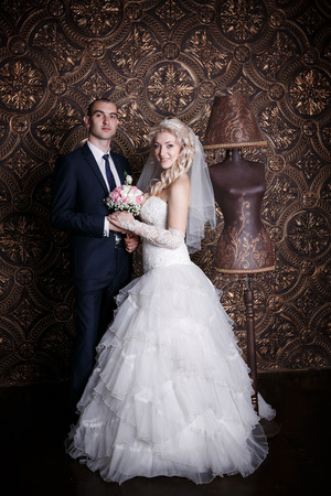 happy groom and the charming bride with a bouquet from roses in studio on a brown backgroundの写真素材