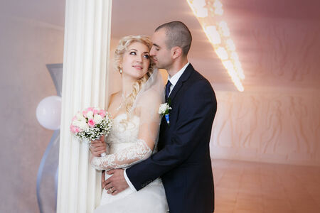 groom and the bride with a wedding bouquet stand near a white columnの写真素材