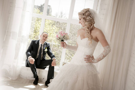 bride with a wedding bouquet from roses and the groom sitting at a window on a backgroundの写真素材