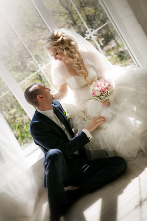 happy groom and the bride sit at a windowの写真素材