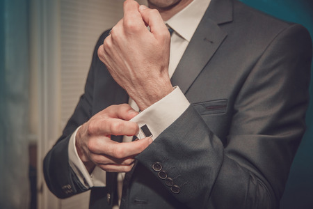 groom putting on cuff-links as he gets dressed in formal wear close upの写真素材