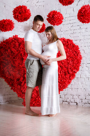 The husband and the pregnant wife on the red heart backgroundの写真素材