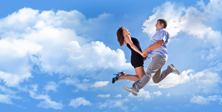 Cheerful loving couple in a jump against the blue sky backgroundの写真素材