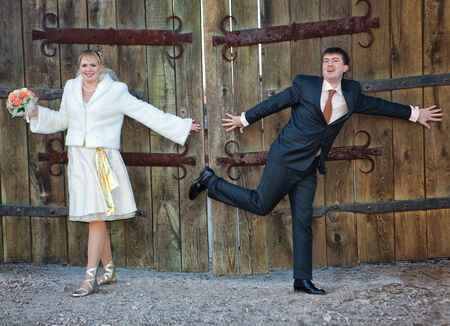 Cheerful groom and the bride stand near wooden gateの写真素材