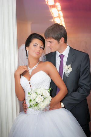 groom and the bride with a wedding bouquet stand near a white columnの写真素材