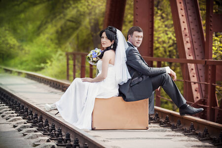 the groom and the bride sit on a suitcase on railway railsの写真素材