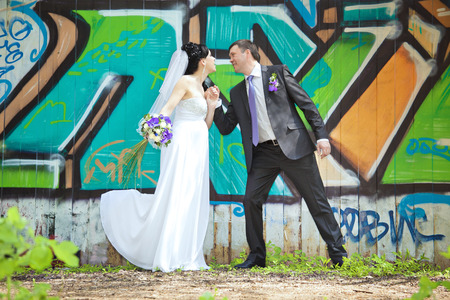 cheerful bride and groom holding hands on graffiti wall backgroundの写真素材