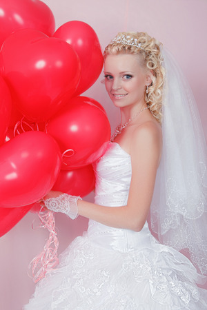 Smiling blonde woman with red balloons in heart shapedの写真素材