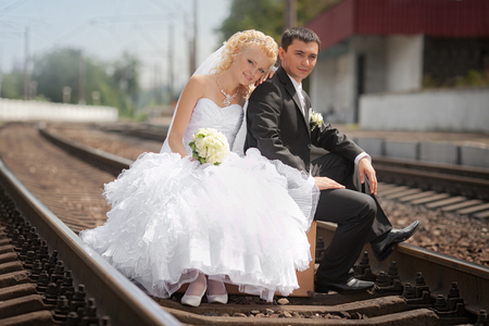 the groom and the bride sit on a suitcase on railway railsの写真素材