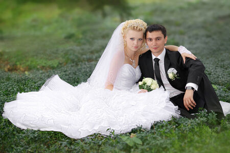 Wedding - Bride and groom hugging and looking in the eyes of one another sitting at a green grassの写真素材
