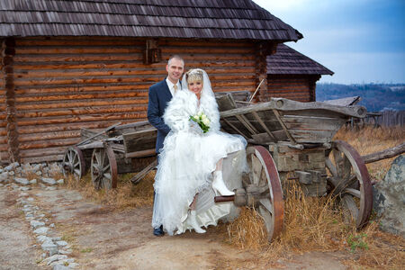 The groom and the bride against the wooden house and an old horse cartの写真素材