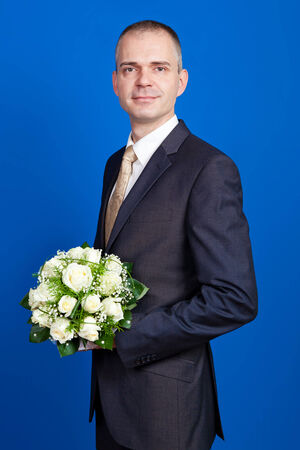 elegant groom holding flowers in a studio on the blue backgroundの写真素材