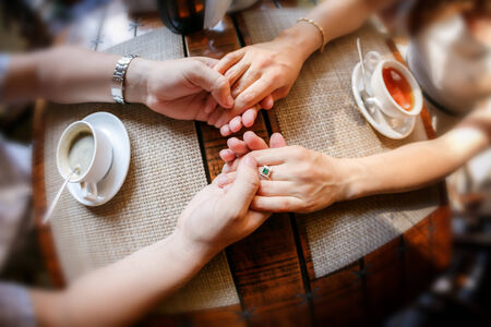 Hands of the guy and hand of the girl at a table with a cup of tea and a cup of coffee in cafeの写真素材