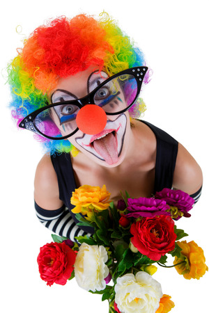Girl in big red glasses and clown costume with a bouquet of flowers puts out the tongue looks up isolated on white background.の写真素材