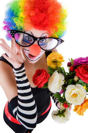 Girl in big red glasses and clown costume with a bouquet of flowers puts out the tongue looks up isolated on white background.の写真素材