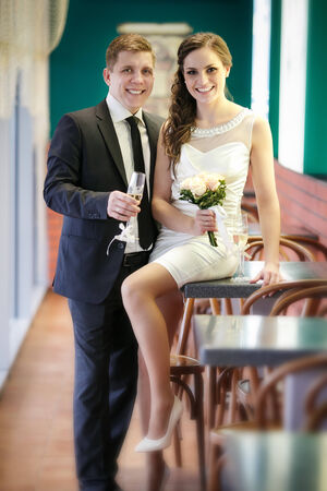 groom with a glass of champagne and the bride with a bouquet from roses in cafeの写真素材