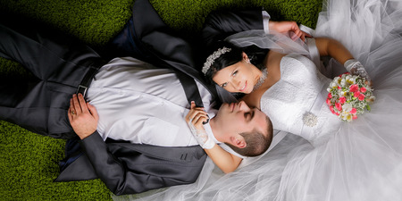 Smiling bride and groom lying on the grass-like carpet.の写真素材