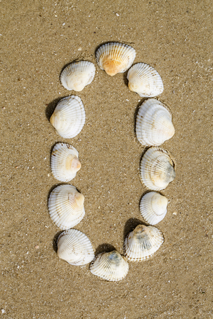 Letter of alphabet makes from seashells on the sand backgroundの写真素材