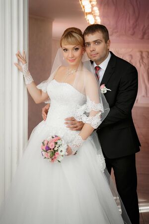 groom and the bride with a wedding bouquet stand near a white columnの写真素材