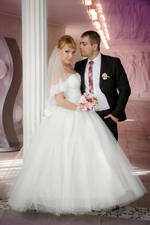 groom and the bride with a wedding bouquet stand near a white columnの写真素材