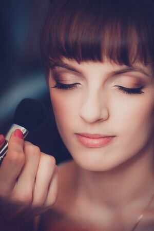 Young beautiful girl applying make-up by make-up artist close upの写真素材