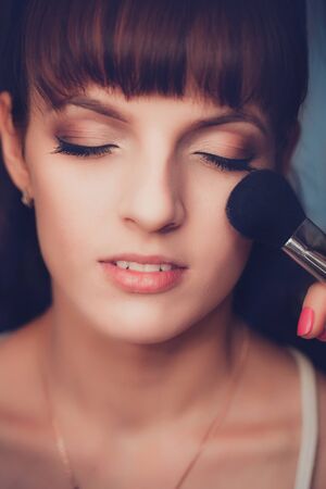 Young beautiful girl applying make-up by make-up artist close upの写真素材