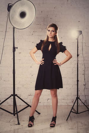 girl in a black dress stands in studio on the a white brick wall backgroundの写真素材