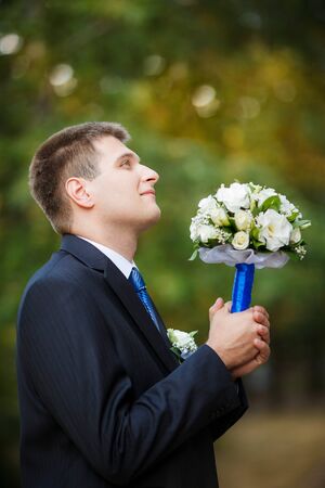 The groom holds a wedding bridal bouquet in hand and looks upの写真素材