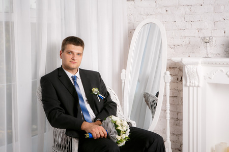 The groom with a wedding bouquet is sitting in the chairの写真素材