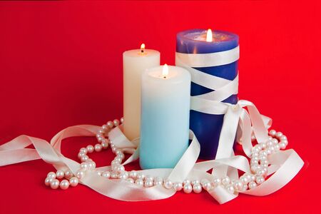 Three burning candles with a tape and a pearl beads on the red backgroundの写真素材