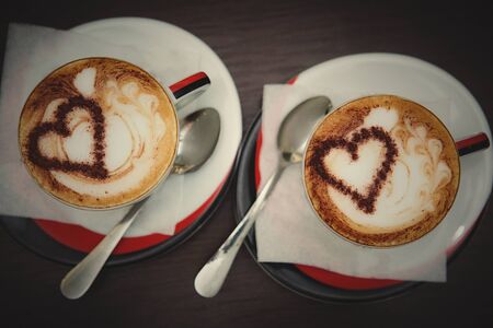 Two cups of coffee with heart pattern in a white cups on wooden background. Love concept.の写真素材