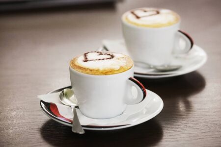 Two cups of coffee with heart pattern in a white cups on wooden background. Love concept.の写真素材
