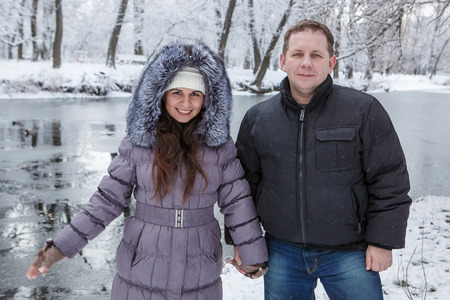 A man and woman are standing near river in snowy park on winter dayの写真素材