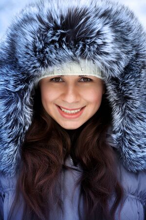 Portrait of a beautiful winter woman in fur hat is walking in the parkの写真素材