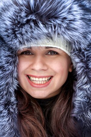 Portrait of a beautiful winter woman in fur hat is walking in the parkの写真素材