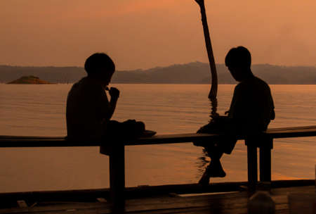 Silhouettes of two children eating lake.の写真素材